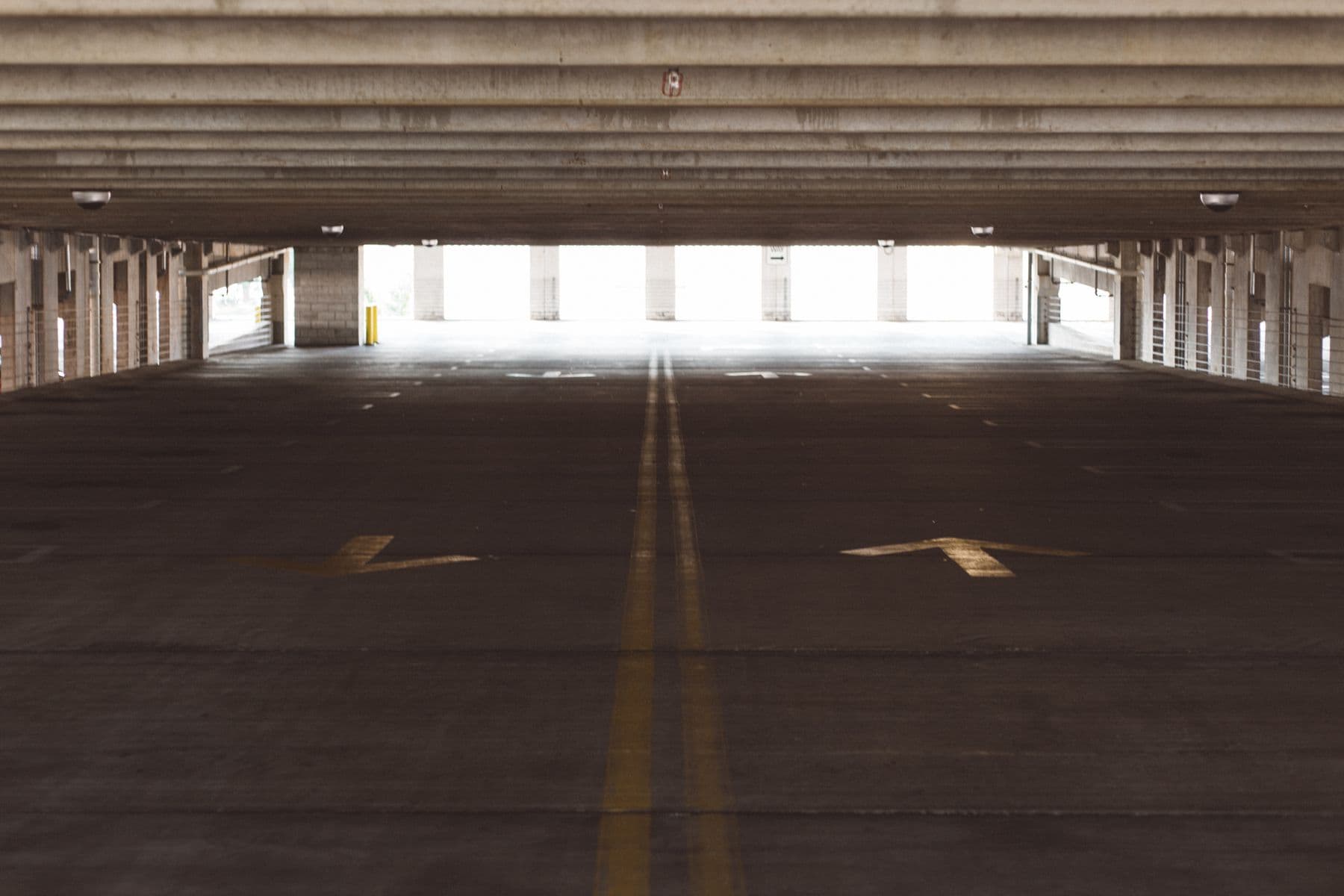 The empty deck of a parking garage with arrows and a yellow center line painted on the floor.
