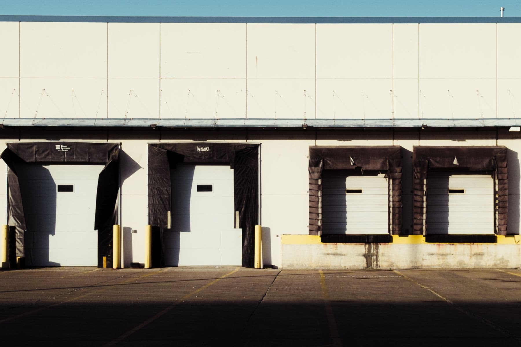 Four loading dock doors along the cream wall of a warehouse, in strong sun.